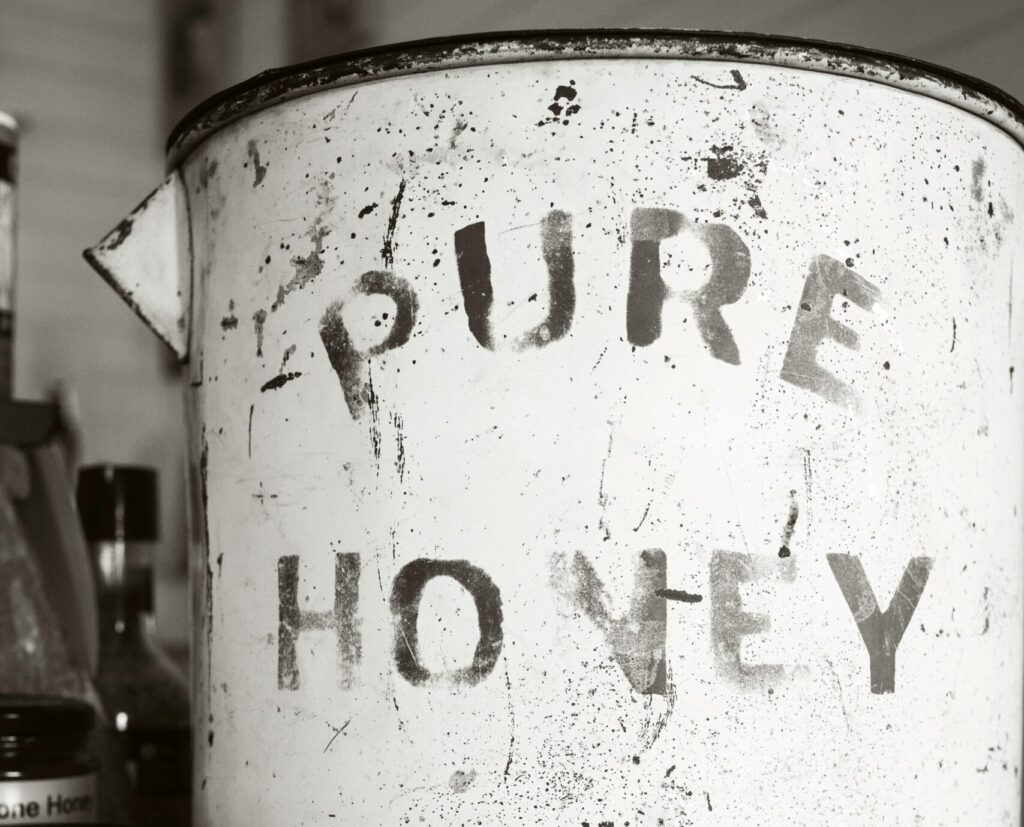 Close-up of an antique, rusty canister labeled 'Pure Honey' surrounded by jars, showcasing vintage charm.