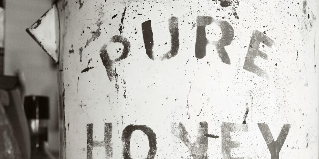 Close-up of an antique, rusty canister labeled 'Pure Honey' surrounded by jars, showcasing vintage charm.