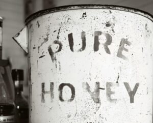 Close-up of an antique, rusty canister labeled 'Pure Honey' surrounded by jars, showcasing vintage charm.